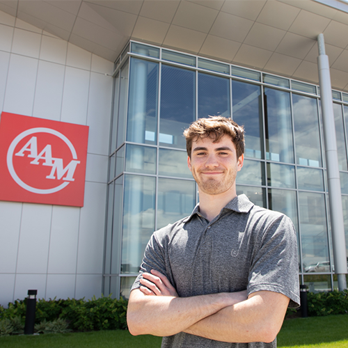 Person standing in front of an AGCO Corporation building, smiling with arms crossed.