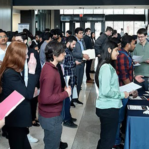 Individuals attending a career fair, interacting and holding documents, in a spacious indoor venue.
