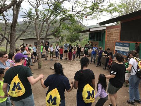 Students with M backbacks standing in circle with younger students in Honduras